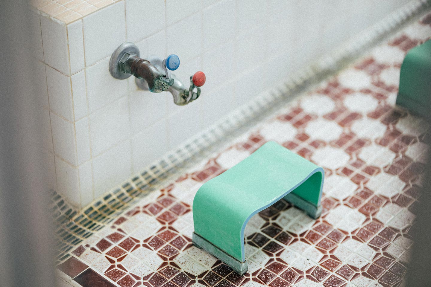 油川温泉浴室の蛇口と、タイル張りの床に置かれた緑の風呂椅子