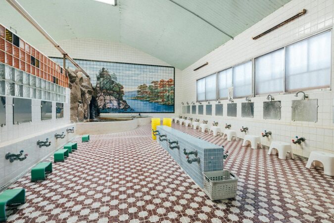 男湯全景。白いタイル張りの壁になっており、奥の浴槽に向かって洗い場が4列、平行に並んでいる。