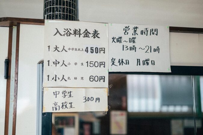 番台に掲示されている、手書きの料金表と営業時間のお知らせ