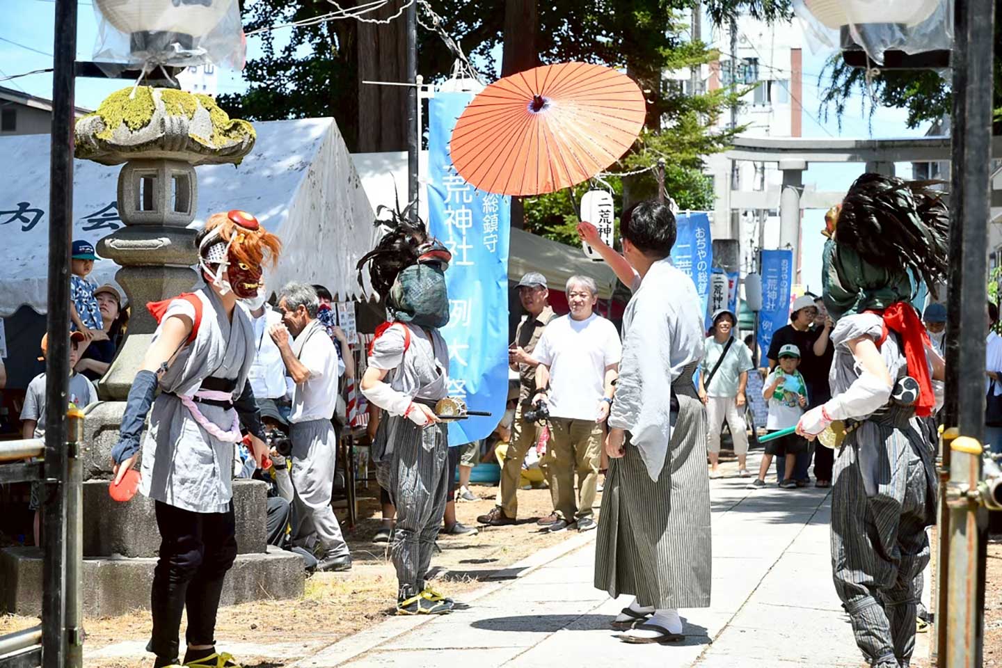 二荒神社祭礼のためお面をかぶる人が境内へ続く道の傍にいる
