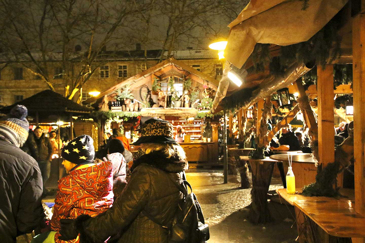 夜のクリスマスマーケットで、帽子を被り温かい格好をした親子がお店の前で楽しんでいる