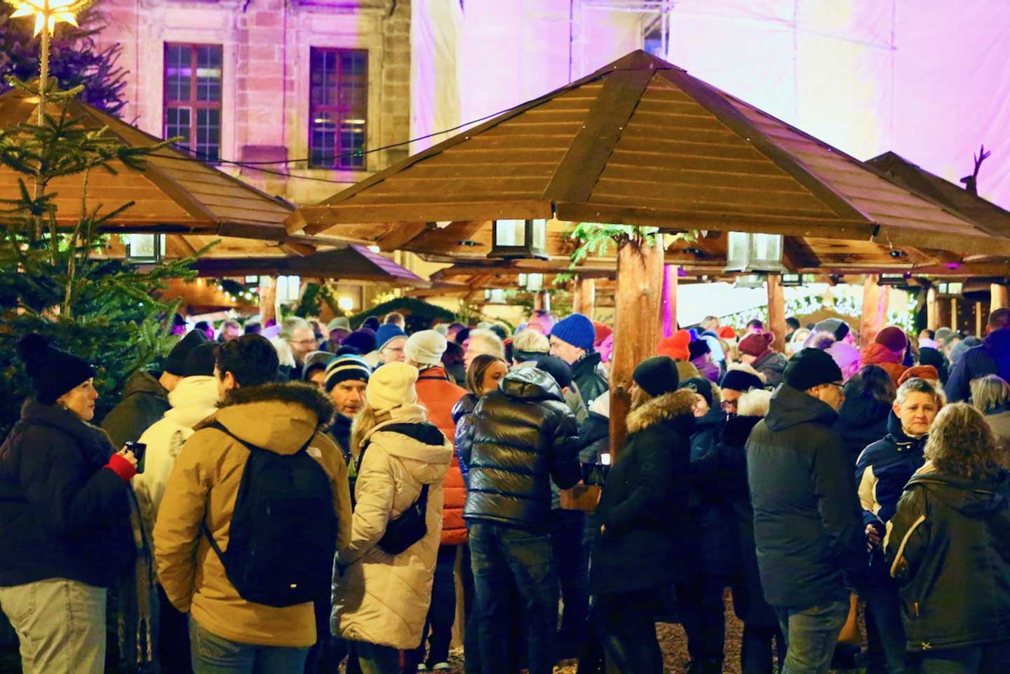 寒空の下、帽子をかぶり、あたたそうな服装でクリスマスマーケットの出店に集い、ホットワインを片手に話し込むたくさんの人々