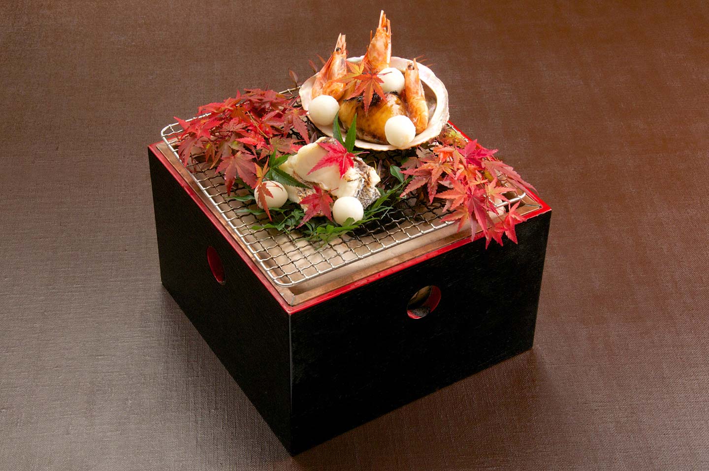 網に乗っている日本料理。えびの頭や刺身に、赤い紅葉の葉っぱが彩りを加えている
