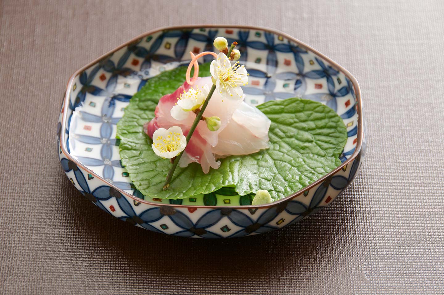 皿の上の刺身。葉わさびと梅の花が添えられている