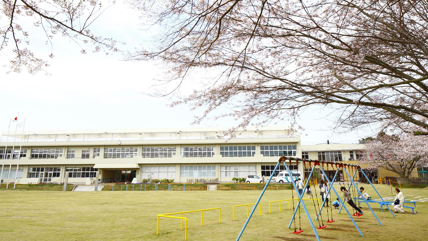 元校庭には芝生が敷かれ、満開の桜の下、子どもたちがブランコやシーソーなどの遊具で遊んでいる