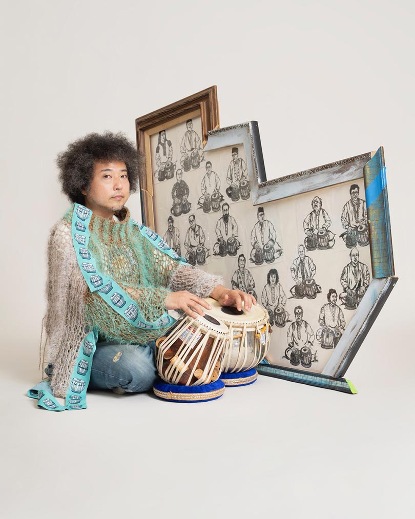 タブラ奏者・U-zhaanさんのポートレート。床に座り、タブラの上に手を乗せている