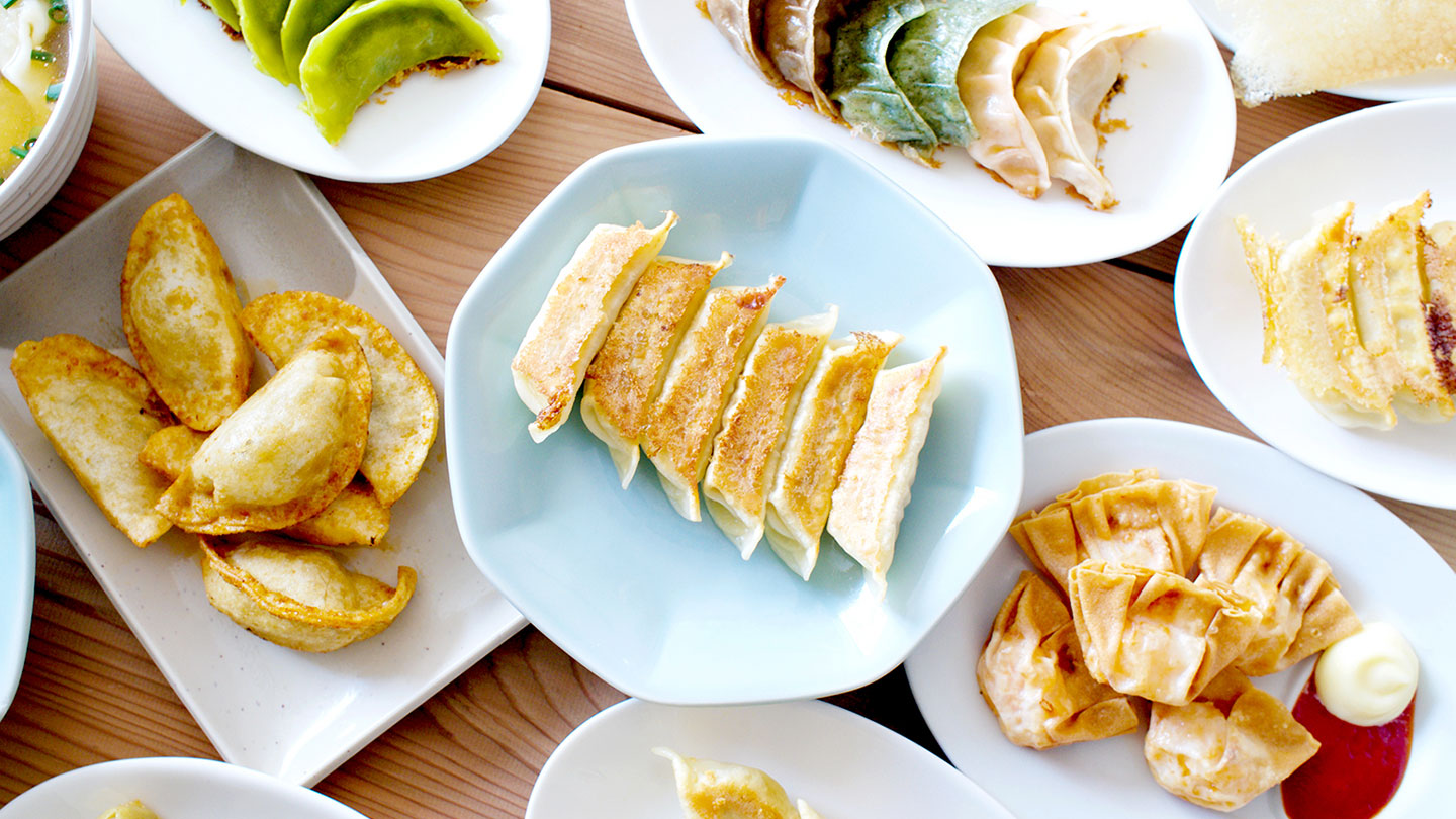 机の上に餃子の皿が並んでいる。定番の餃子や揚げ餃子、緑色の餃子などさまざまな餃子がある