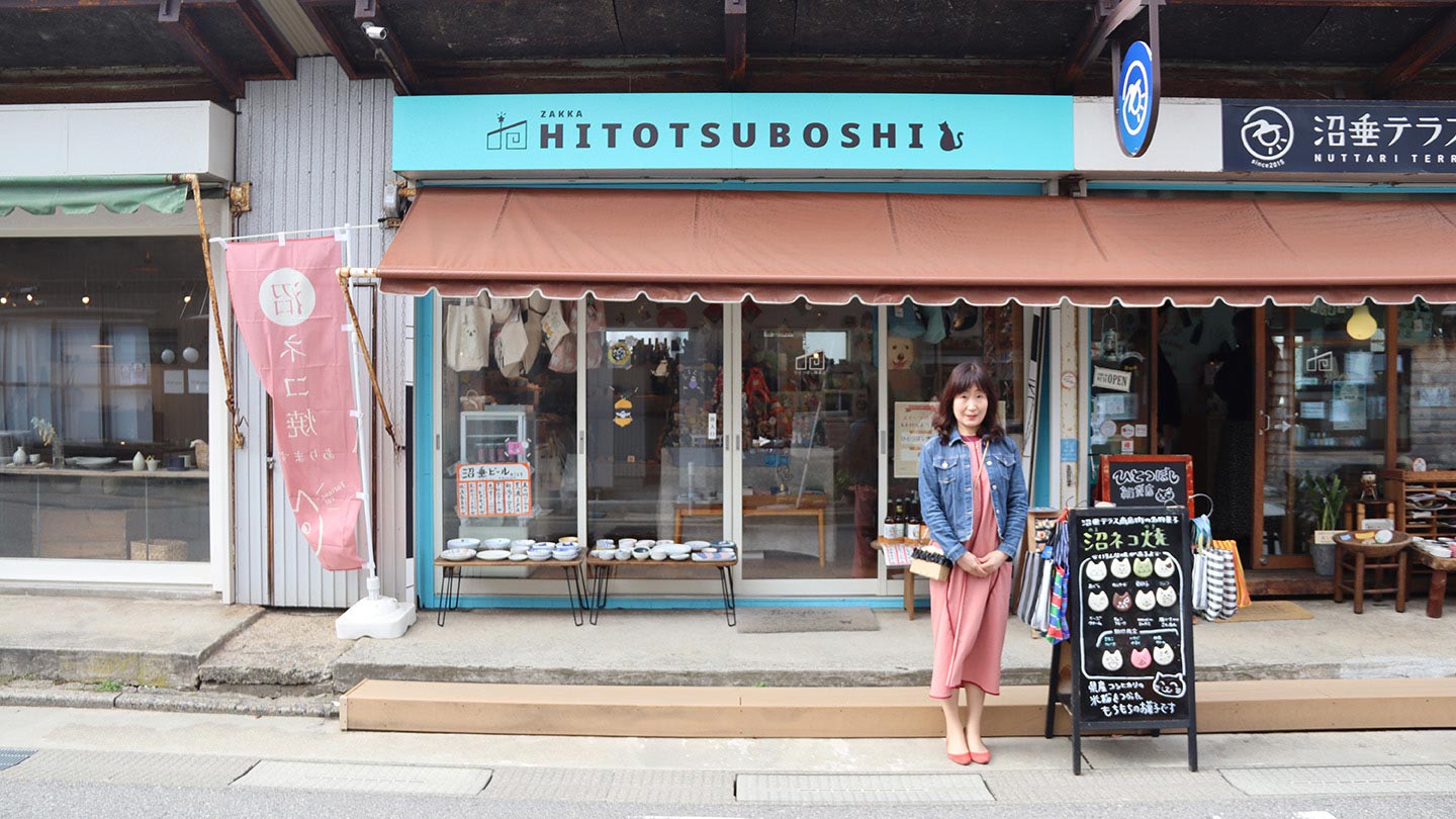 商店街にあるお店の前に立つ女性。その横には「沼ネコ焼」の看板があり奥には店が3軒並んでいる