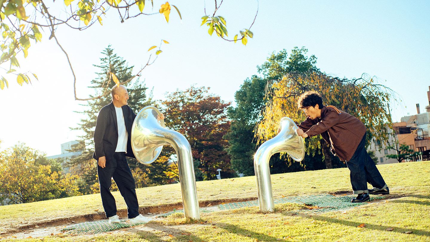 ラッパ状に開いた筒が芝生の広場に2つ生えていて、それぞれの前に鷲田めるろさんと片桐仁さんが立っている