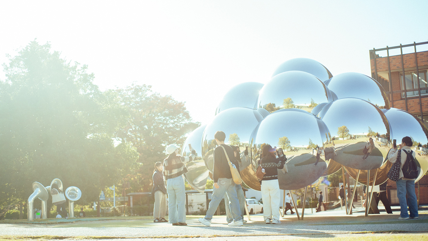 鏡面になった球体16個を集めてつくられた作品『まる』に人が集まっている様子