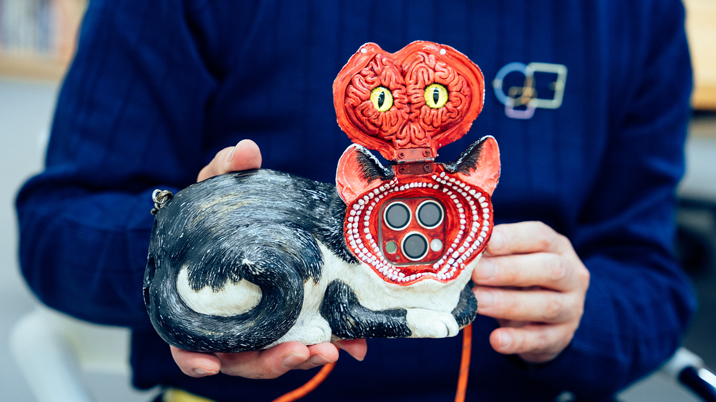 猫のスマホカバーの顔部分を開け、中身のデザインを見せてくる様子