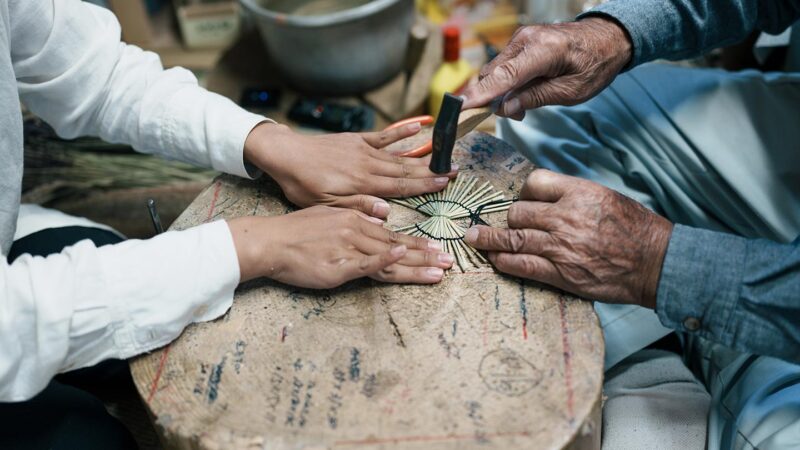 鶴の飾り物を押さえる智香さん。清さんが小さな金づちでわらをたたき、鶴の羽にあたる丸い部分を整える