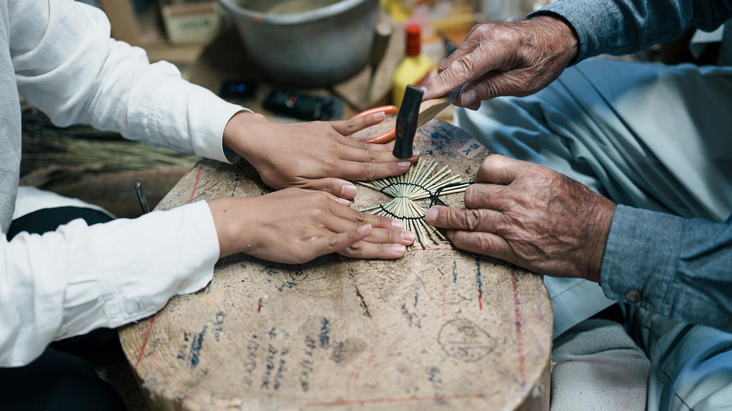 鶴の飾り物を押さえる智香さん。清さんが小さな金づちでわらをたたき、鶴の羽にあたる丸い部分を整える