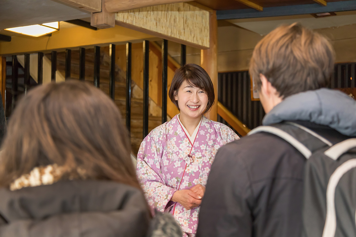 2人の観光客の肩越しに、着物姿で迎える笑顔の女性