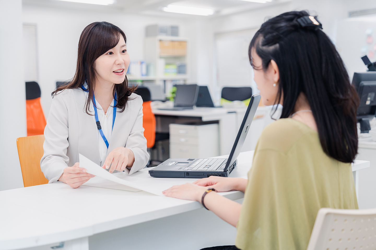 オフィスの受付越しに向かい合い、話をするスーツの女性と、聞いている女性