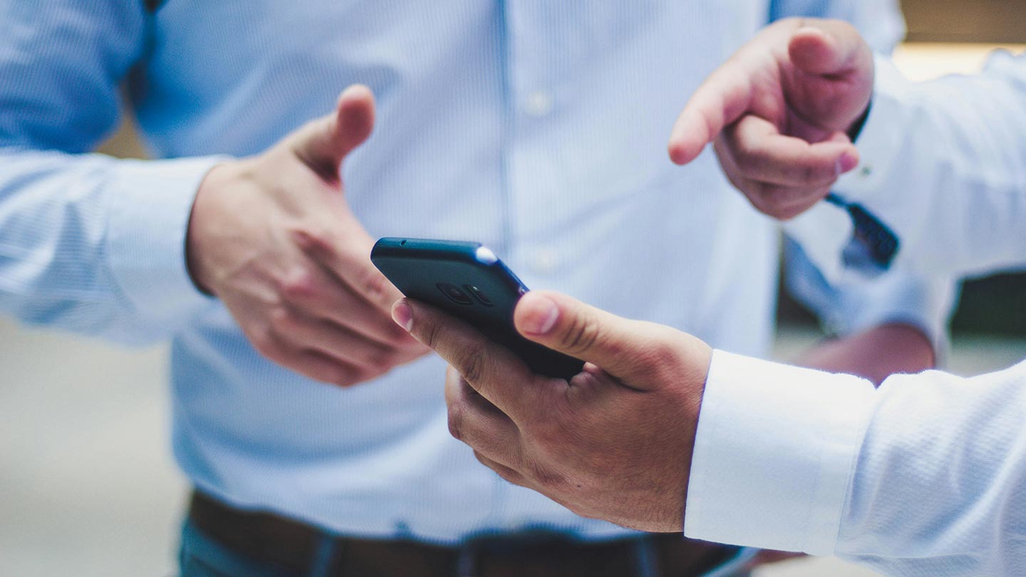 スマホを持って話す男性二人の手元