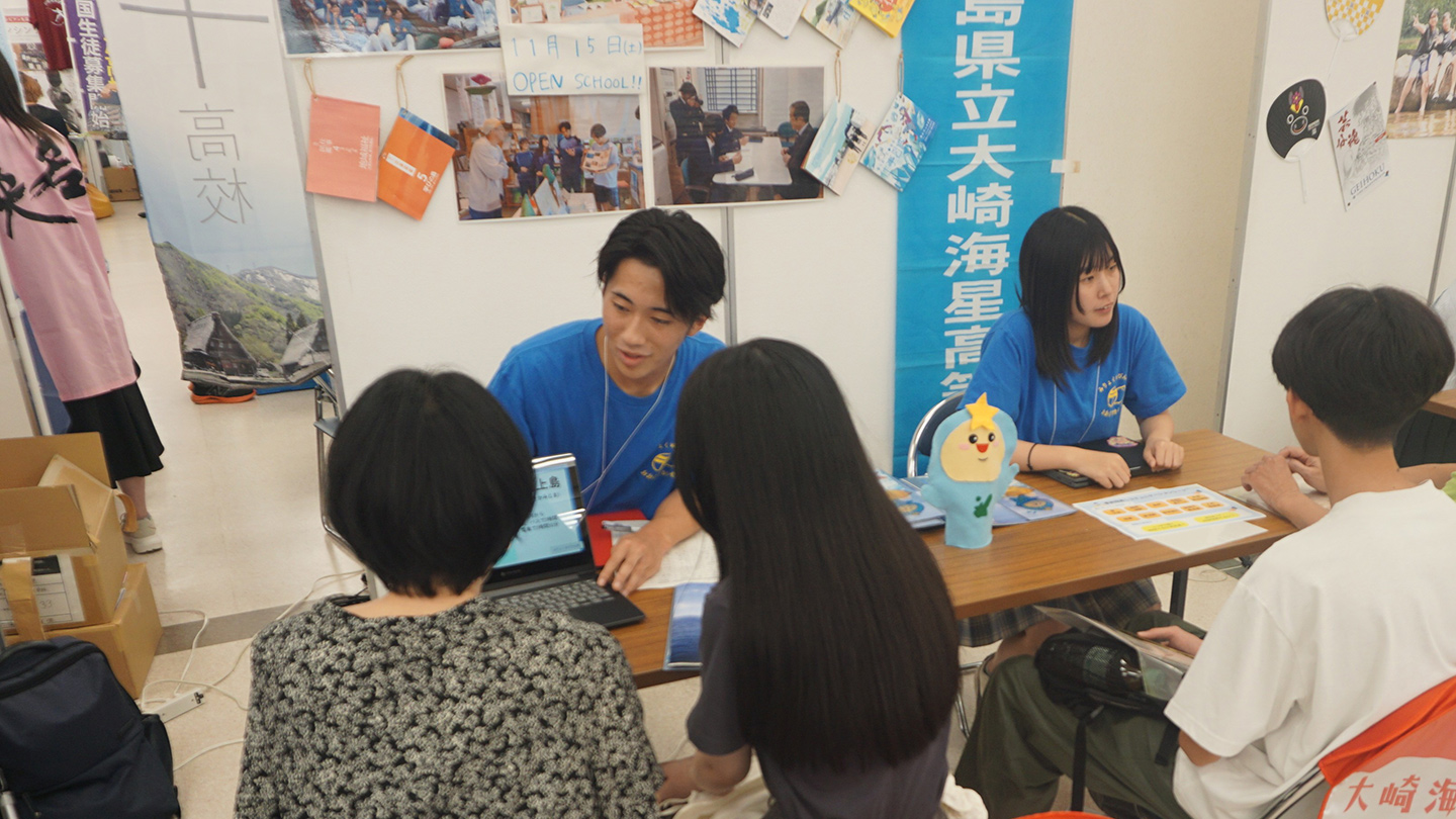 2025年に東京で開催された「地域みらい留学」高校進学フェスの大崎海星高校ブース。2人の生徒が親子に向かって学校の説明をしている