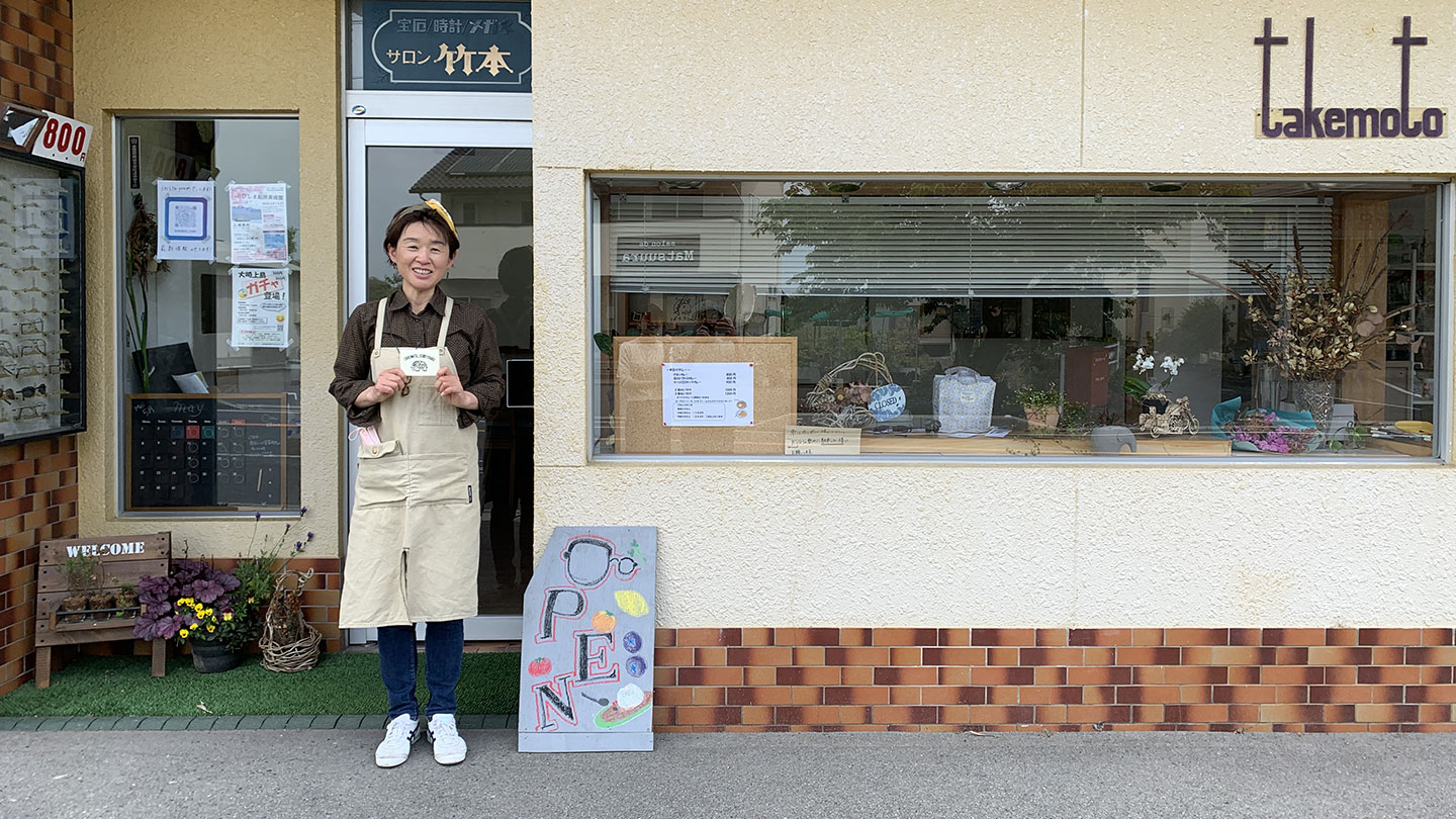 窓が大きく設置された「タケモトカレー」の外観。「OPEN」と書かれた看板と、その横に店主が立っている