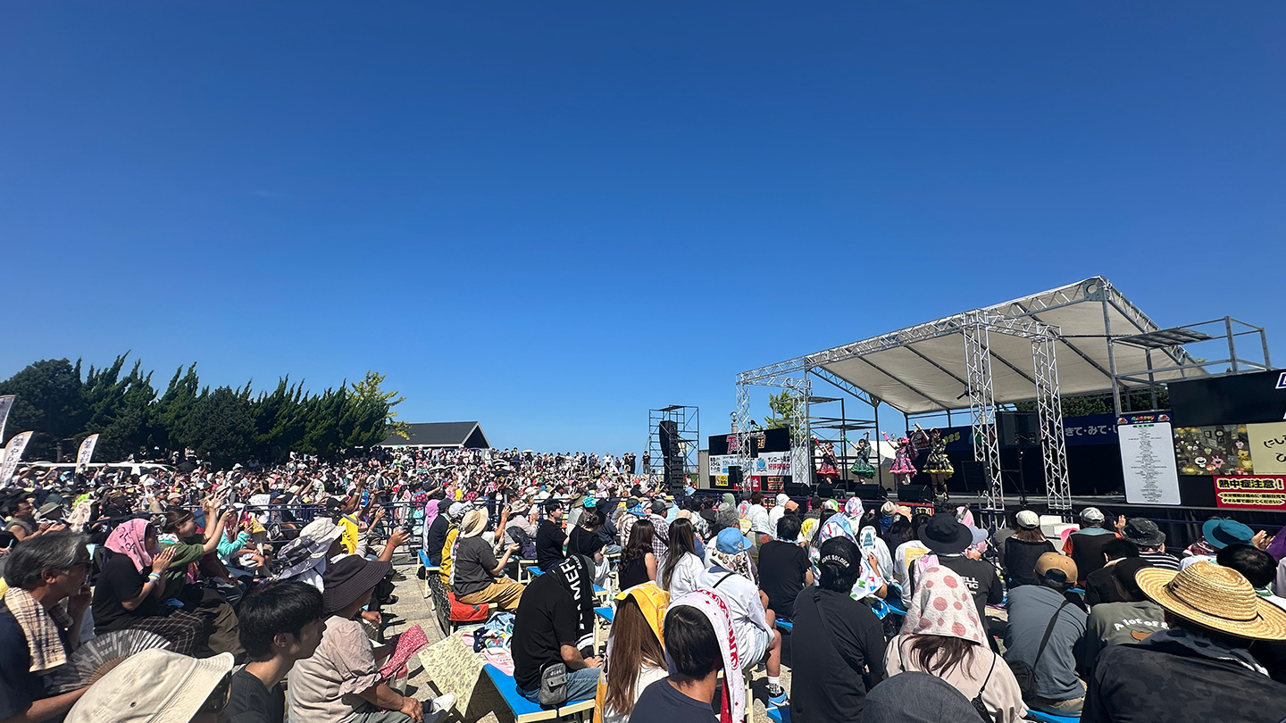 青い空の下で大勢の観客の前でパフォーマンスをするりんご娘