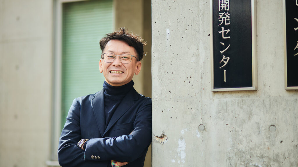 腕組みして笑顔を見せる、信州大学 学術研究院 教育学系 准教授の佐藤和紀さん