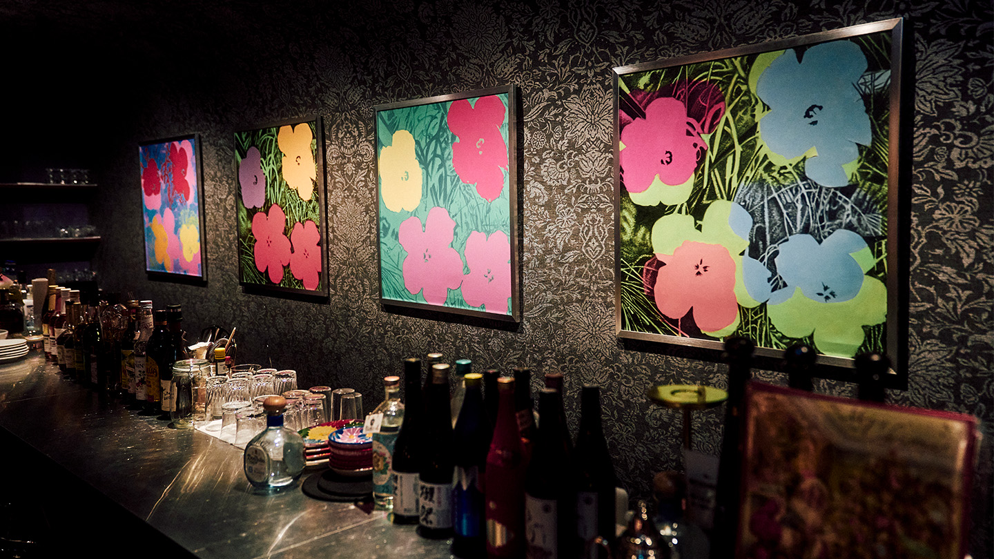 黒い壁にカラフルな花の絵が4枚飾られているバーカウンター