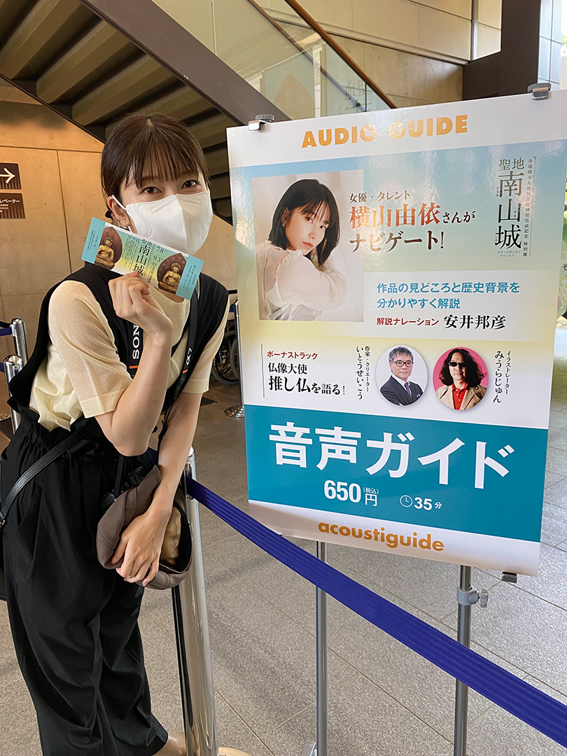音声ガイドの案内パネルの前で、チケットを手にポーズをとる横山由依さん
