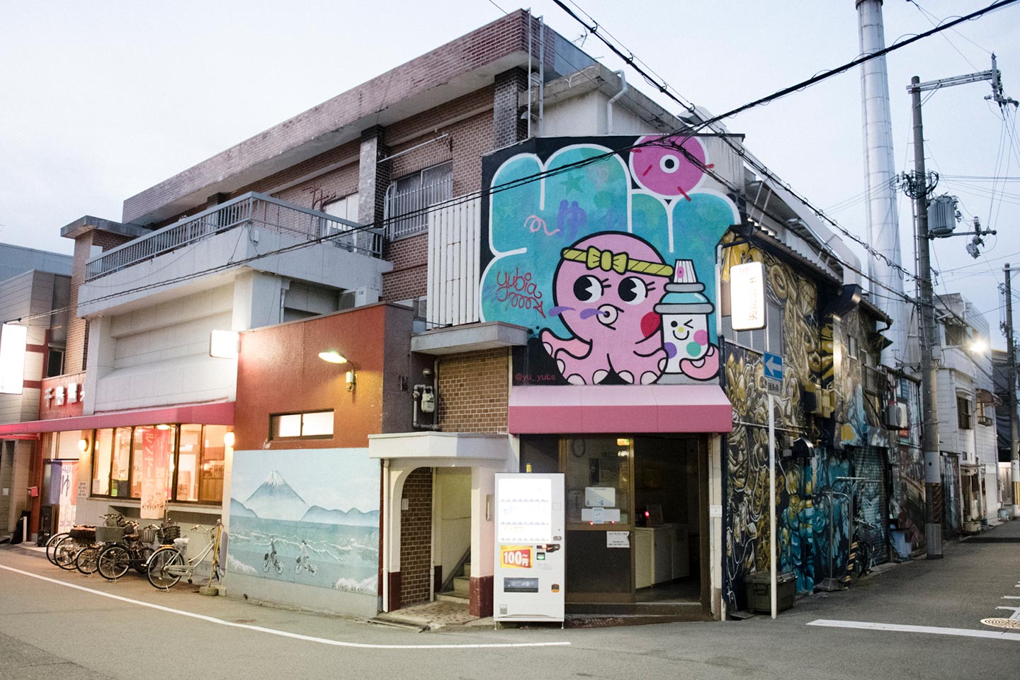 千鳥温泉の壁面に、鉢巻を頭に巻いたピンクのタコの絵と、山を背景に自転車を漕ぐ人の絵などが描かれている