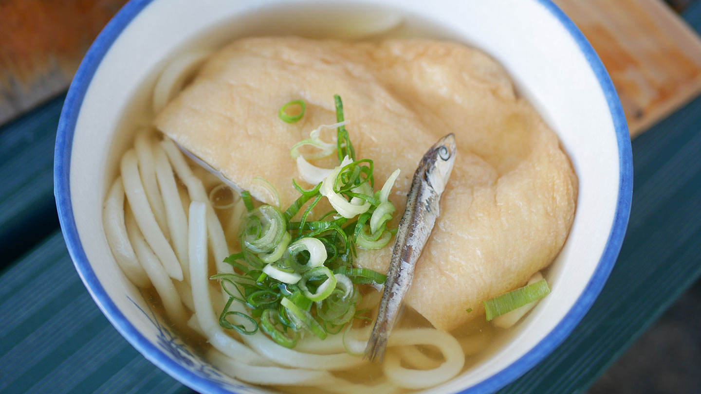 透き通ったおつゆのなかにうどん、そのうえにいりこ、お揚げ、青ネギが乗っている