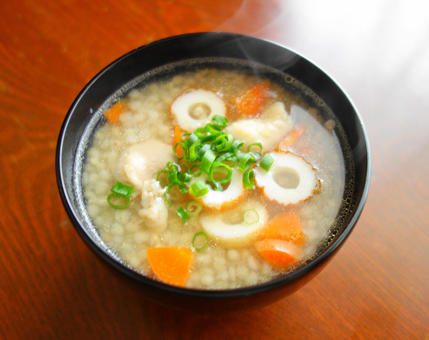 汁のなかにそばの粒、ちくわ、にんじん、鶏肉が入り、上には青ネギがのっている