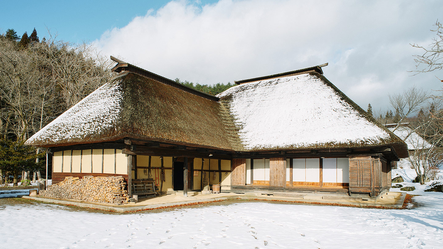茅葺屋根に雪がうっすら積もった木造一軒家の外観