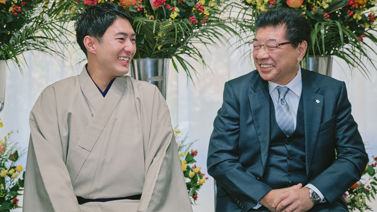 公演祝いとして贈られたスタンド花を背景に笑う橋之助さんと石田会長