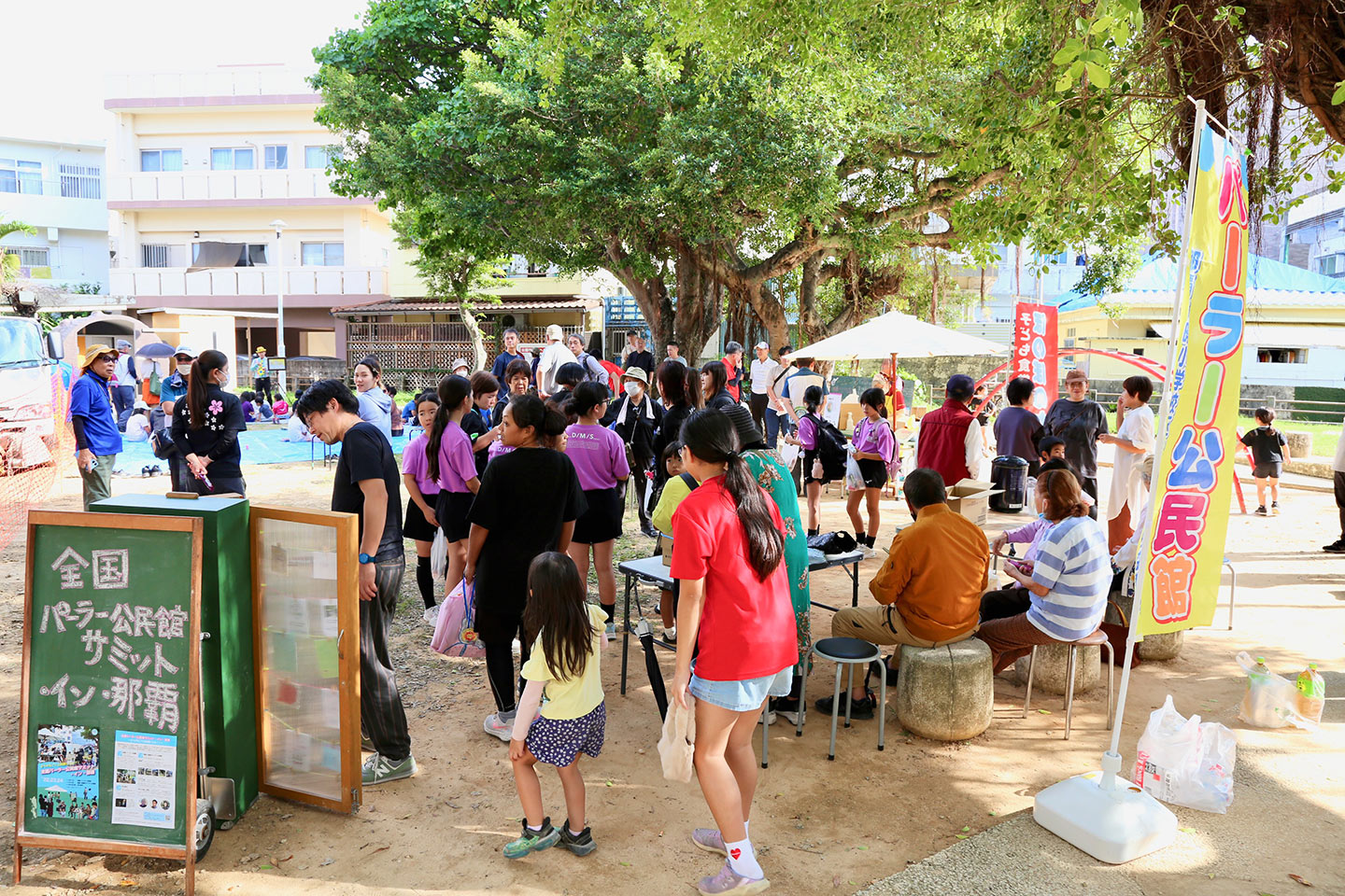 広場にパラソルとテーブル、椅子が用意され、人々が集っている