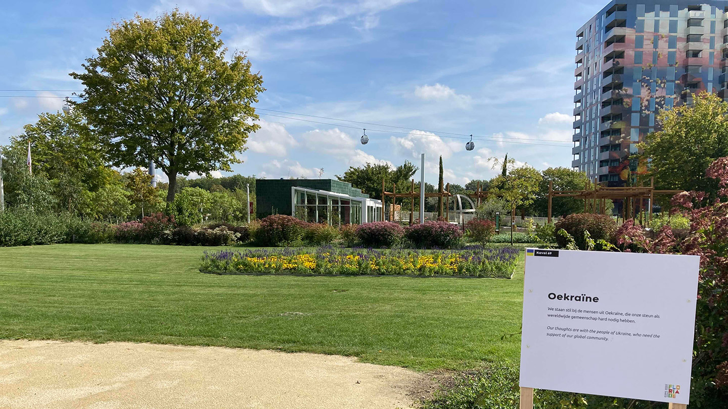 青と黄色の花で国旗を表した花壇と説明看板が立つ様子