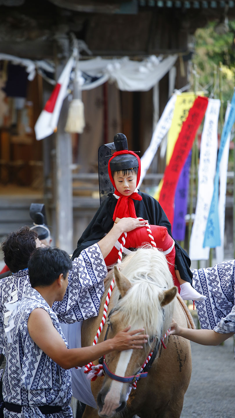 馬に乗る着物を着た7歳の男の子。両脇から大人が支えている