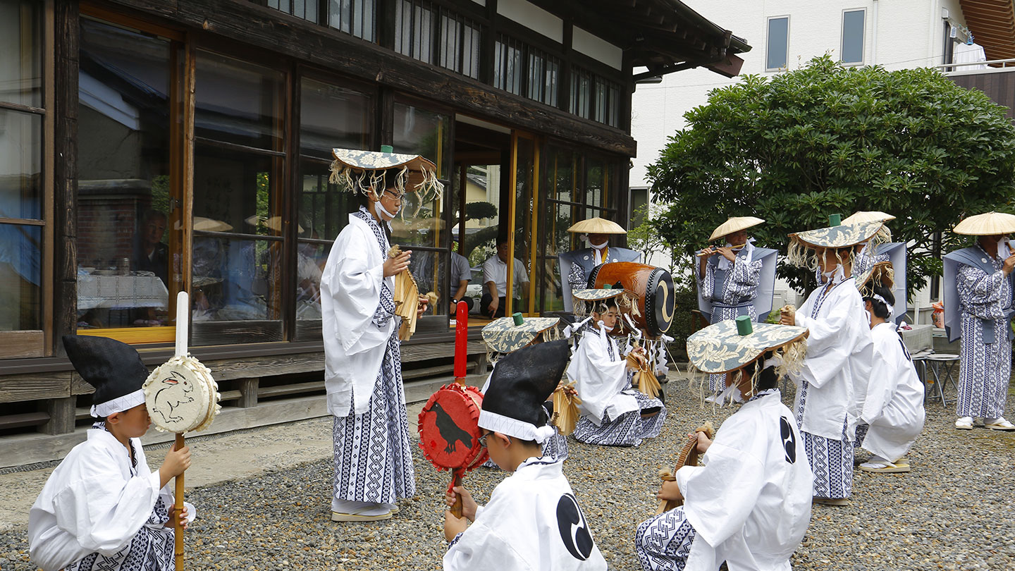 装束をまとい、太鼓などの楽器を持って座ったり立ったりしている子どもたち