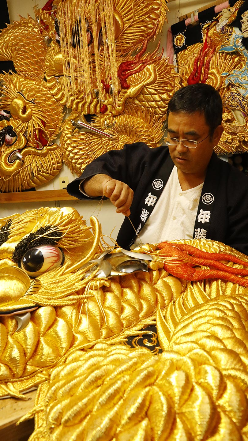 金色の糸で紡がれた巨大な龍の刺繍と、それを手掛ける法被を着た男性