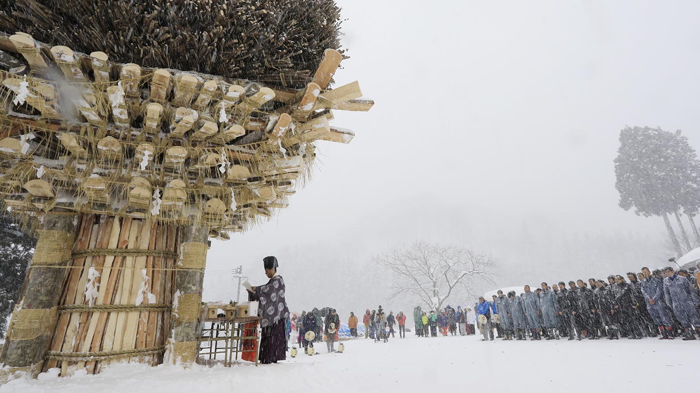雪景色のなかに立つ、木材などで組み上げられた社殿。祈りを捧げる神主と、それを見守る男たち
