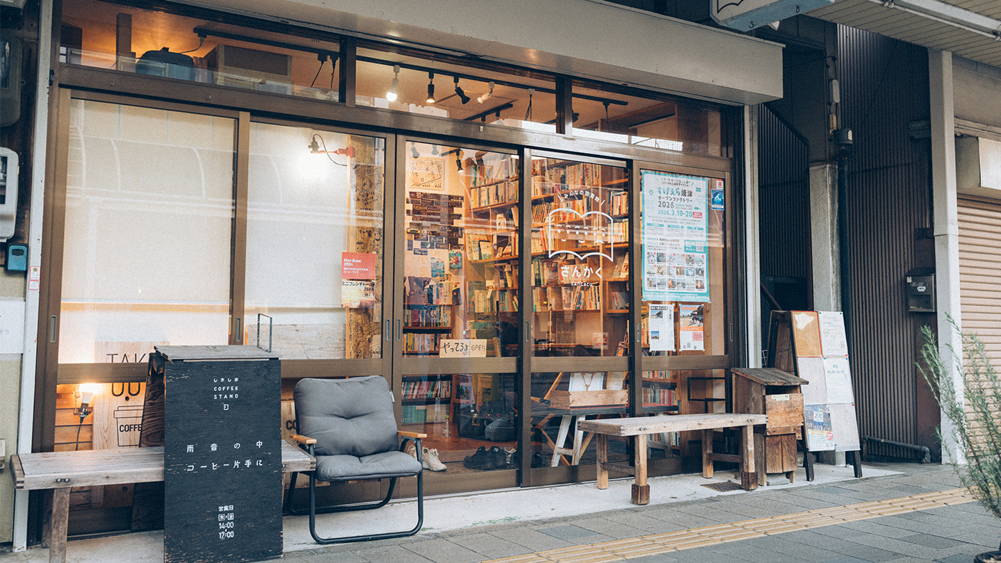 商店街に面した「みんなの図書館 さんかく」の外観。ガラス越しに本棚が見え、入口前にベンチや看板が置かれている