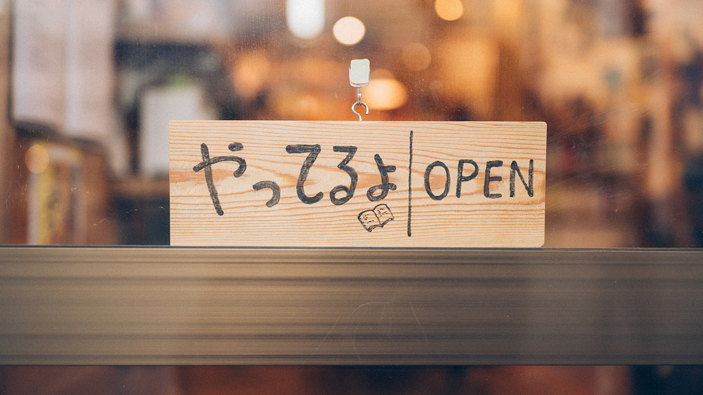 木製の「やってるよ／OPEN」と書かれた営業中サインがガラス扉にかかっている
