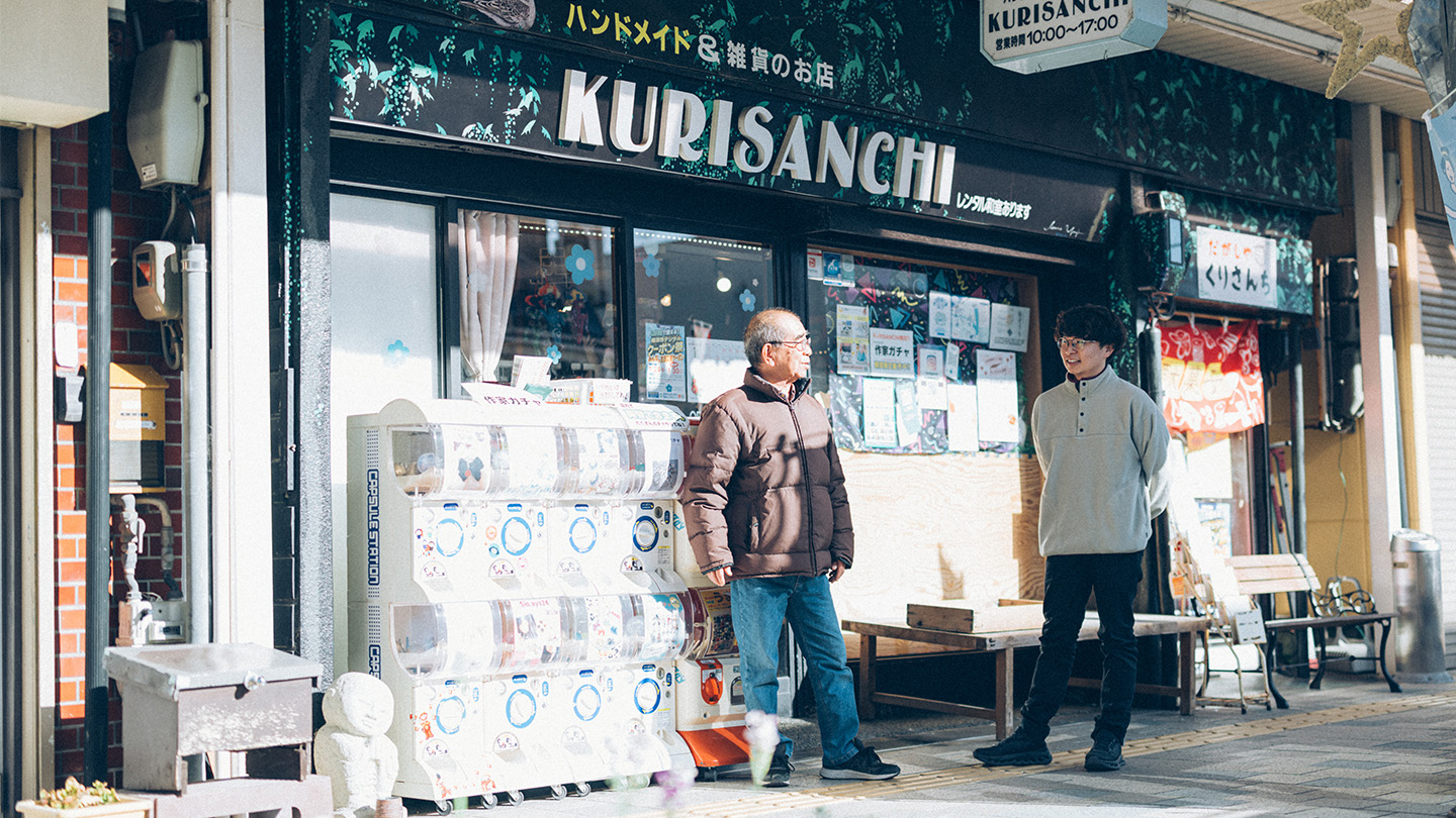 商店街の店舗「KURISANCHI」の前に立ち、土肥さんと栗下さんが会話している様子