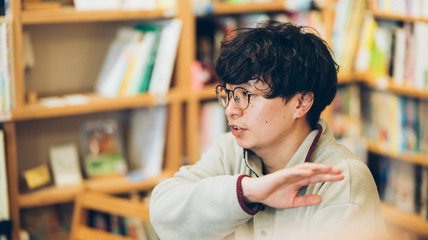 本棚を背景に話している土肥さんの横顔