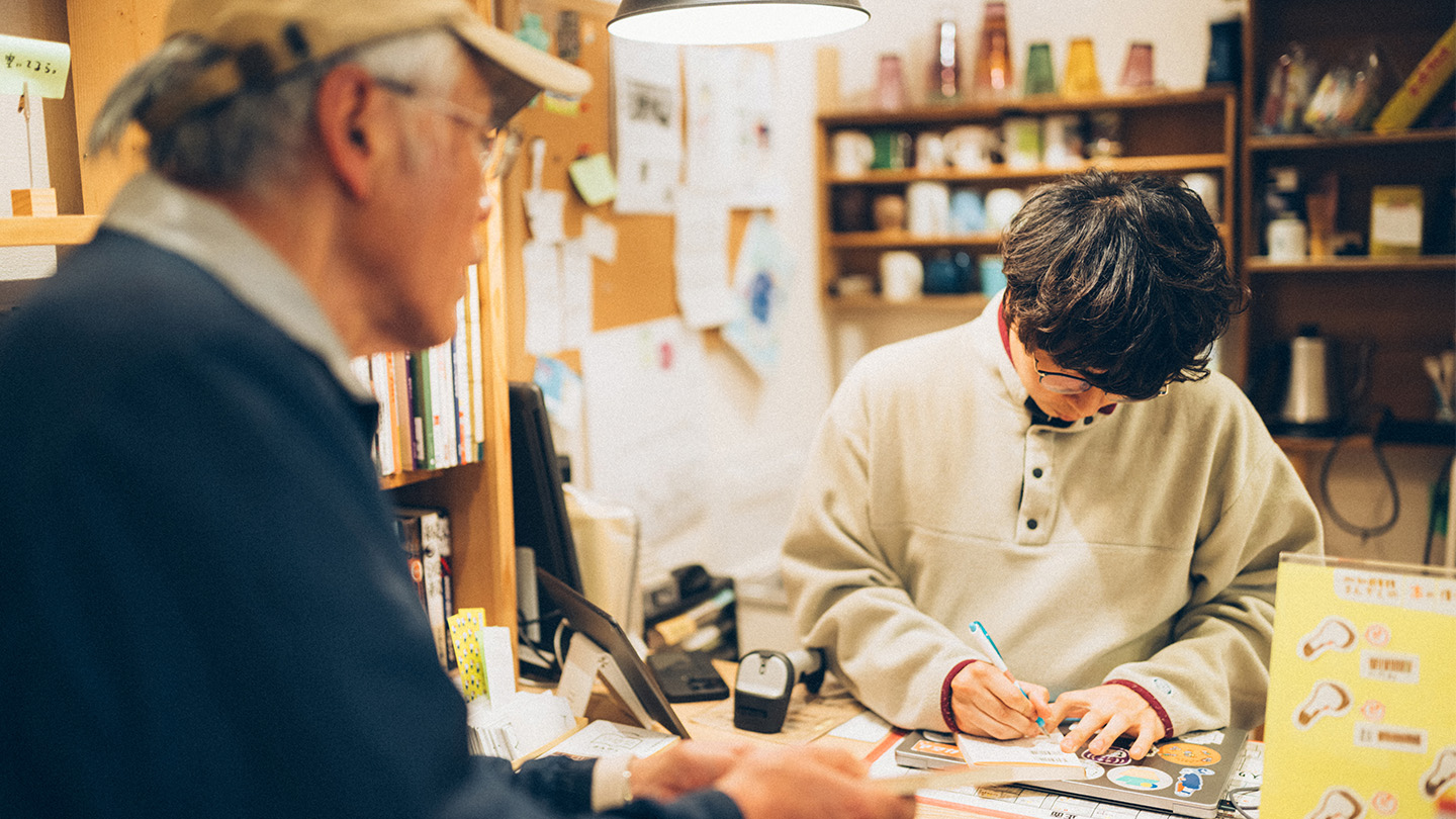 利用者の男性に対し、カウンター内の土肥さんが貸し出し用紙を記入している様子