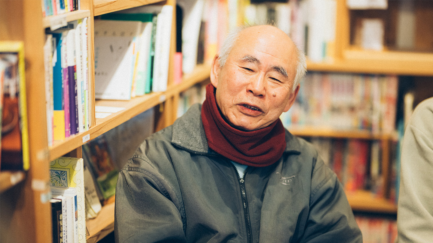 本棚を背景に、椅子に座った村松さんが笑顔で話している様子