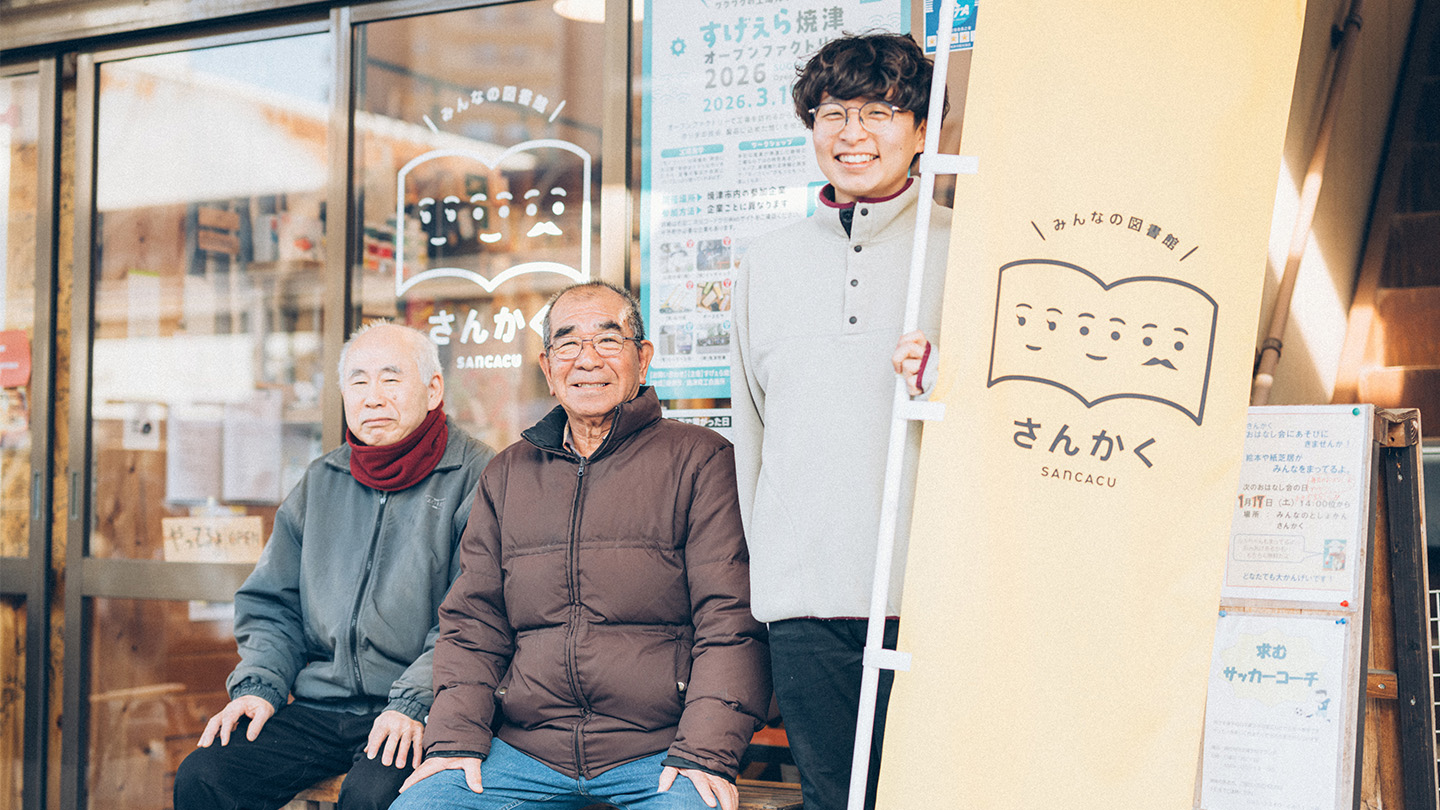 商店街の店舗前で、取材を受けた3人が並ぶ様子。背後のガラス扉には「みんなの図書館 さんかく」のロゴが見える