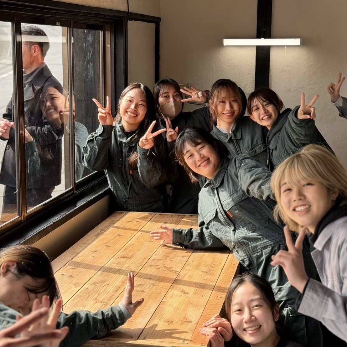 おそろいのつなぎを着てピースなどのポーズを取り写真に映る学生たち