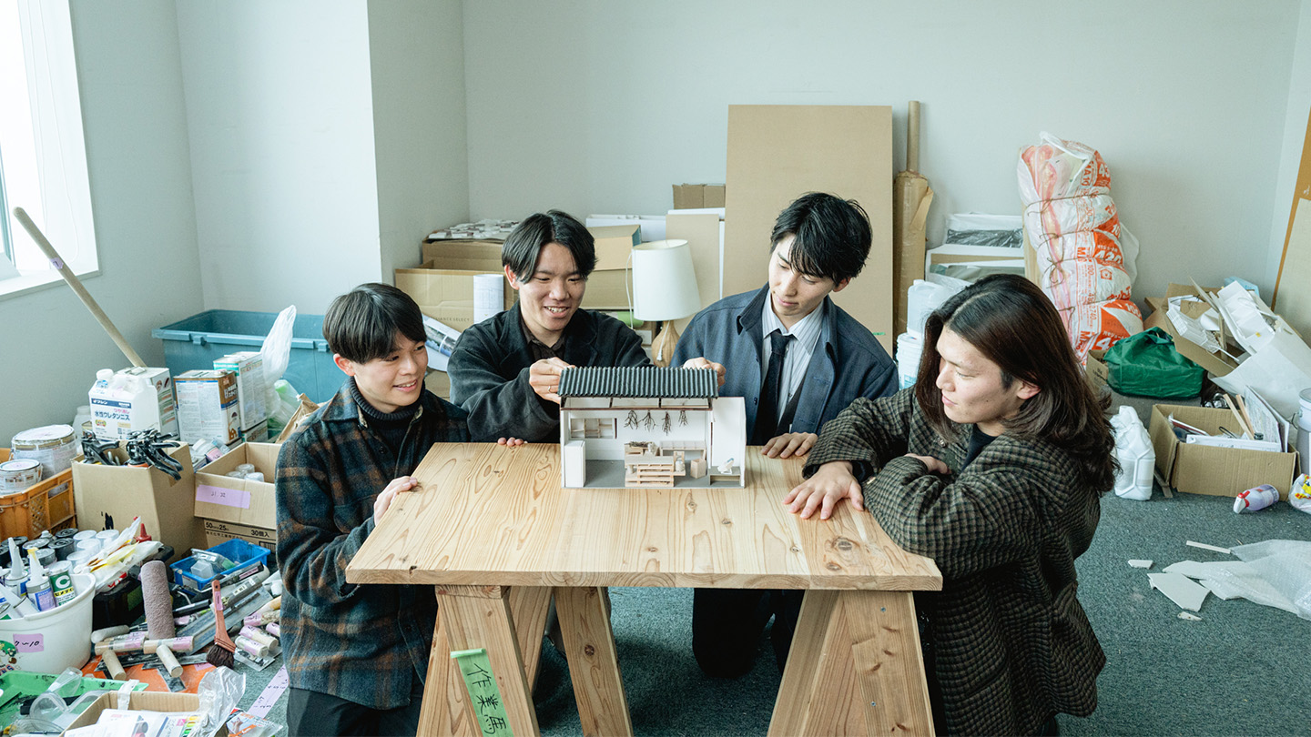部室の真ん中に木製のテーブル。その上に置かれた小さな家の模型を、4人が囲んで眺めている