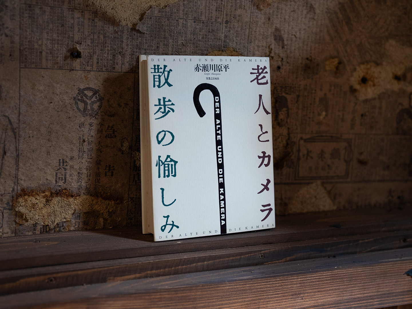 新聞紙を貼ったような古い壁に、赤瀬川原平『老人とカメラ 散歩の愉しみ』が立てかけてある