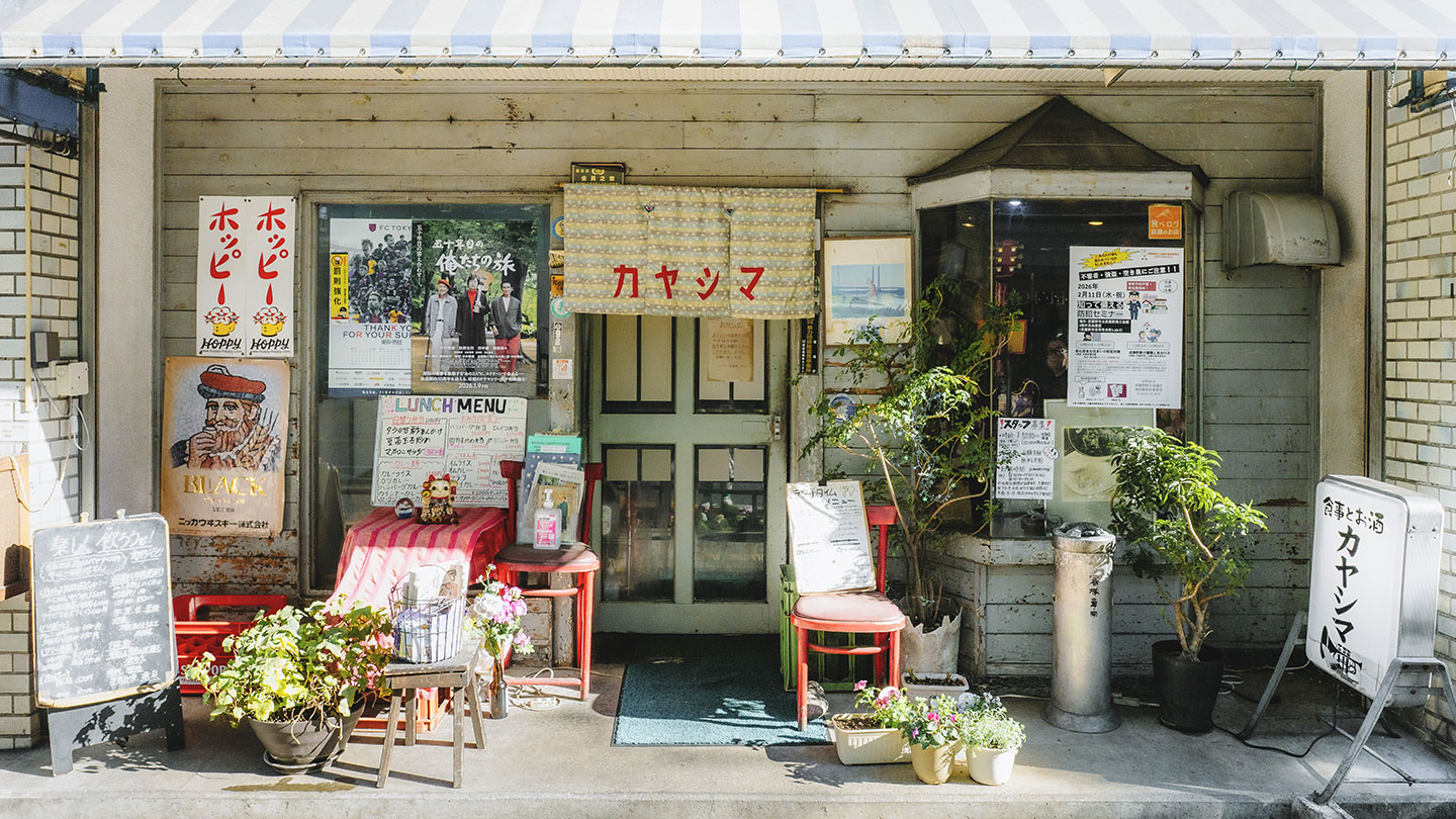 喫茶店「カヤシマ」の外観。暖簾のある入口前にメニュー看板や鉢植えが並ぶレトロな店構え