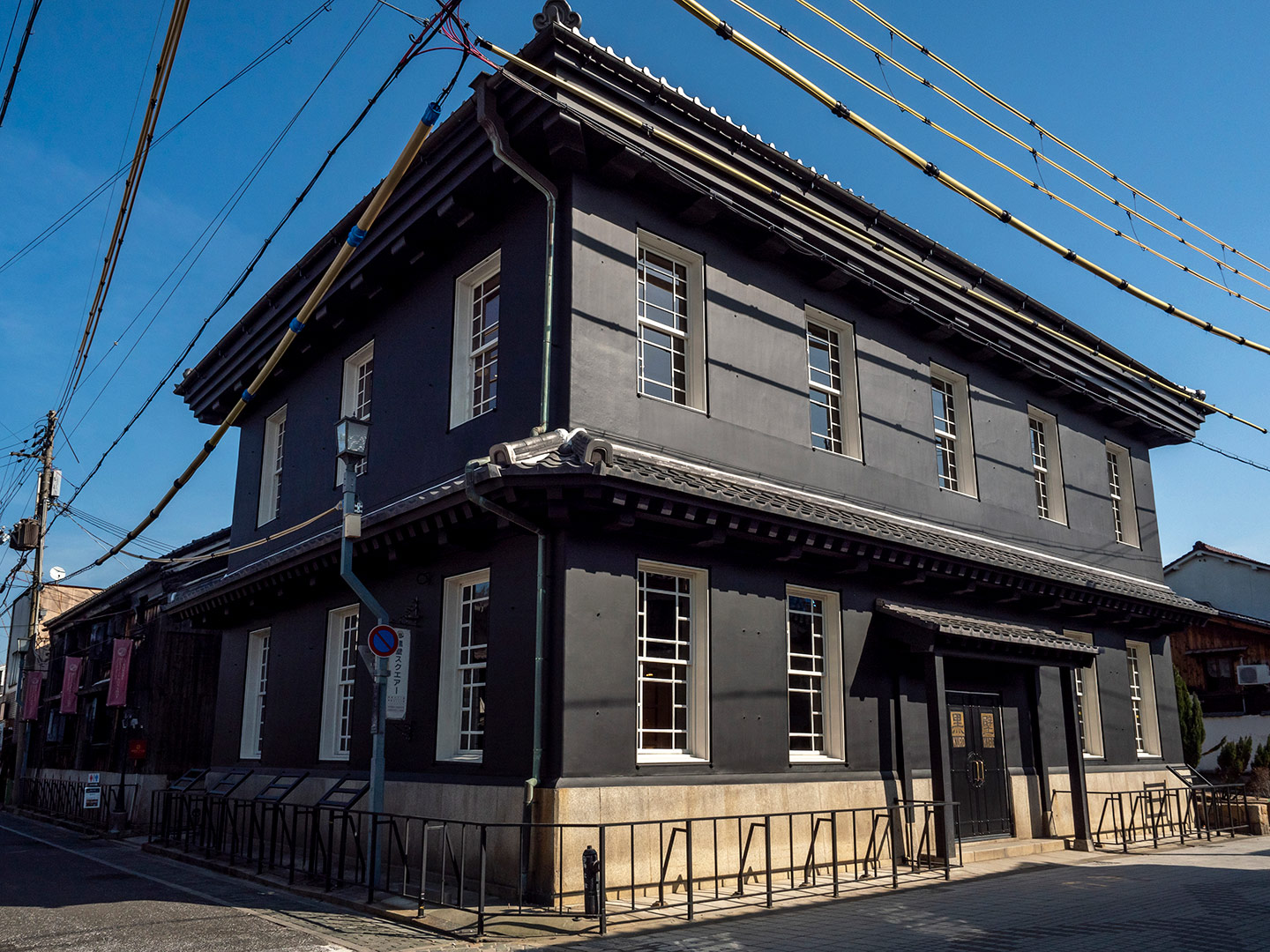 黒い外壁が特徴的な黒壁ガラス館本館の外観。洋風の窓が並ぶ2階建ての歴史的建物が、青空の下の街角に建っている