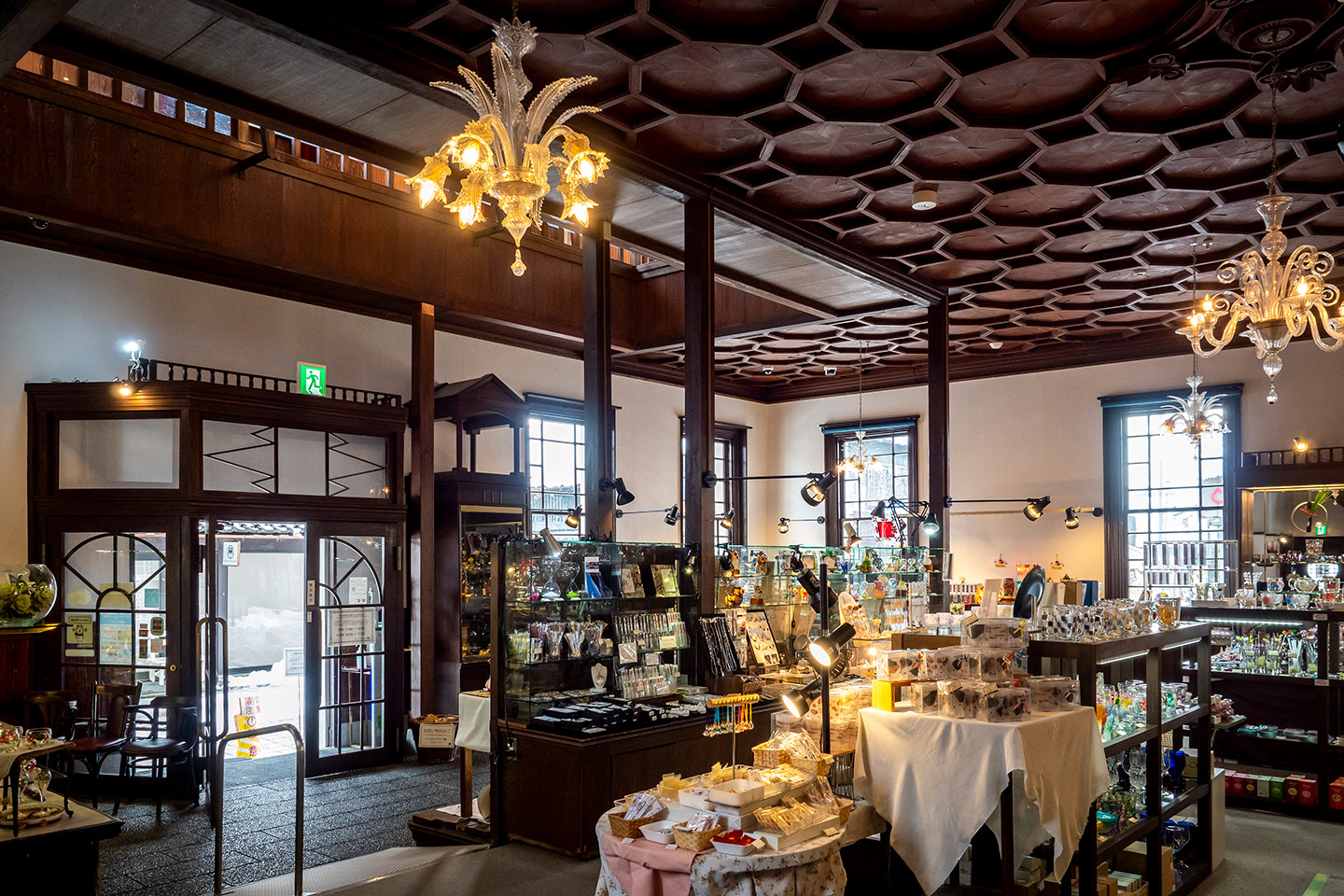 黒壁ガラス館本館の内観。シャンデリアが灯るクラシックな空間に、ガラス製品が並ぶ展示棚やテーブルが配置されている